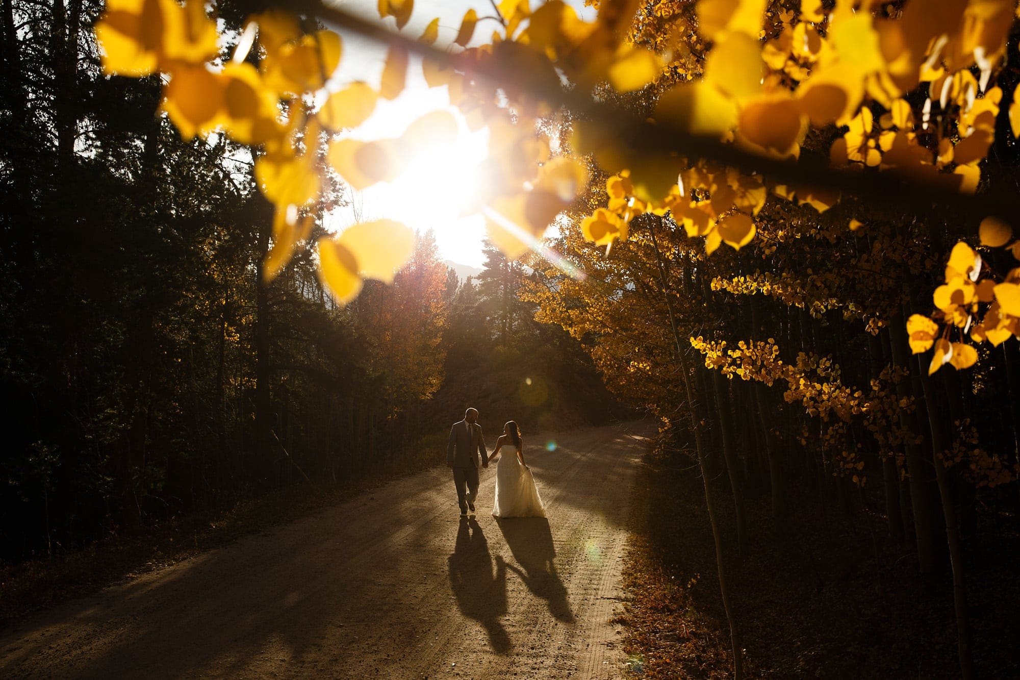 Frank and Heidi walk along a dirt road as the golden aspen trees are illuminated by the setting sun on Boreas Pass near Breckenridge during their wedding