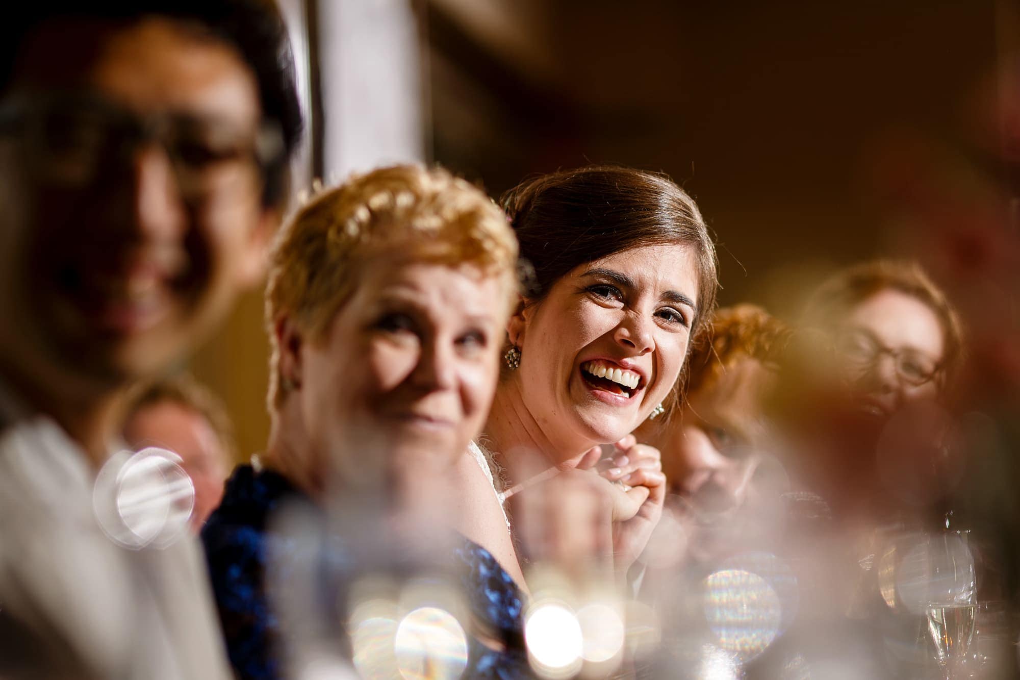 A bride laughs while her brother goves a toast during the reception at Rembrandt Yard in Boulder