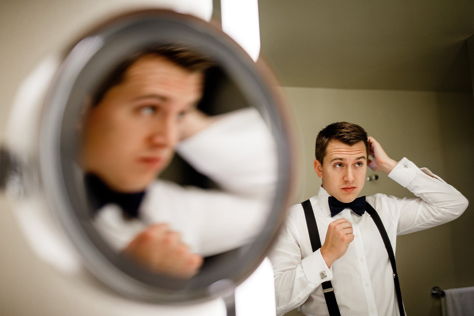 A groom is reflected in a parobolic mirror while fixing his hair at a hotel in Chicago.
