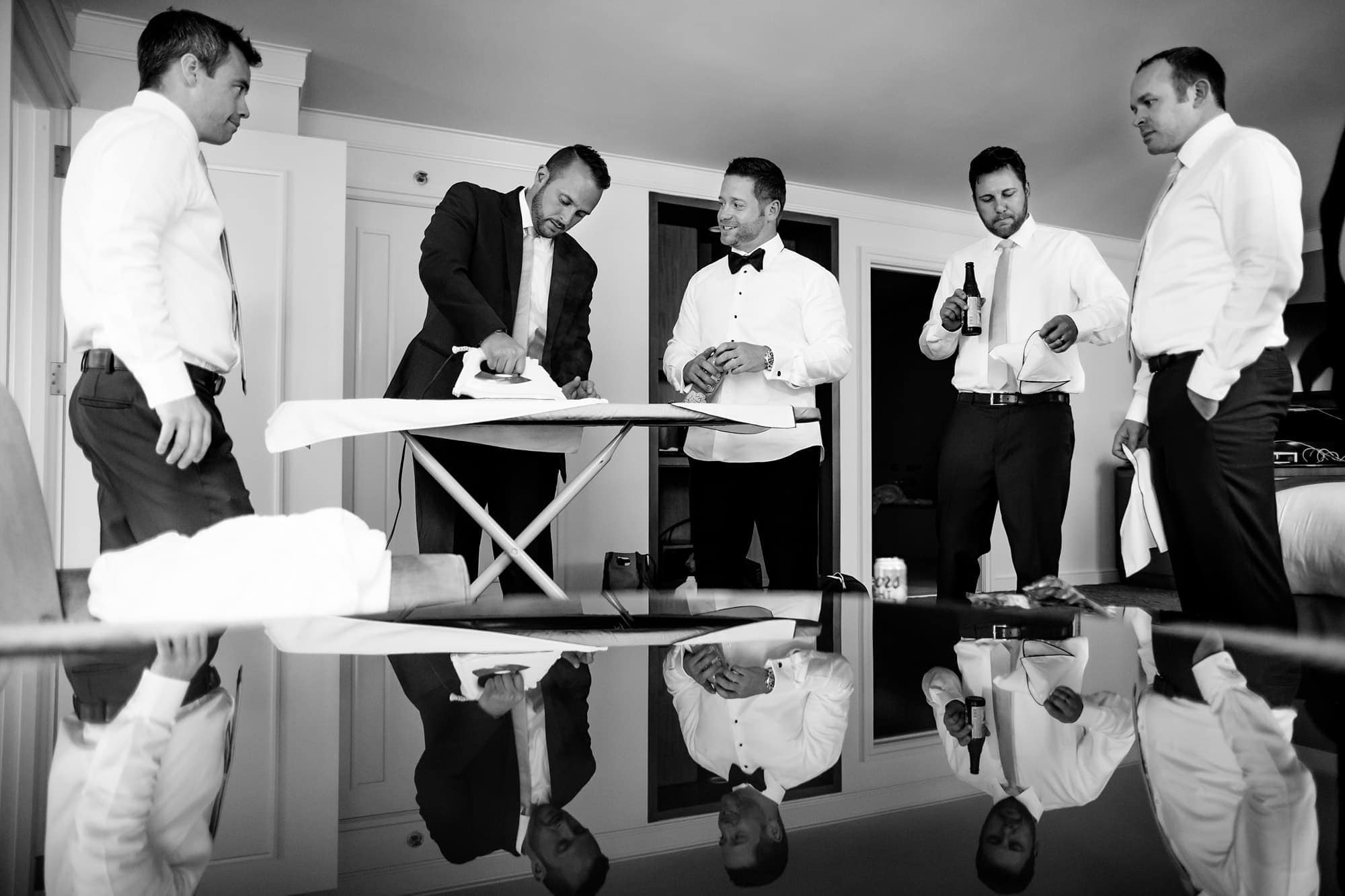 A group of groomsmen help the groom with some ironing while drinking beer inside a hotel in Chicago before the wedding.