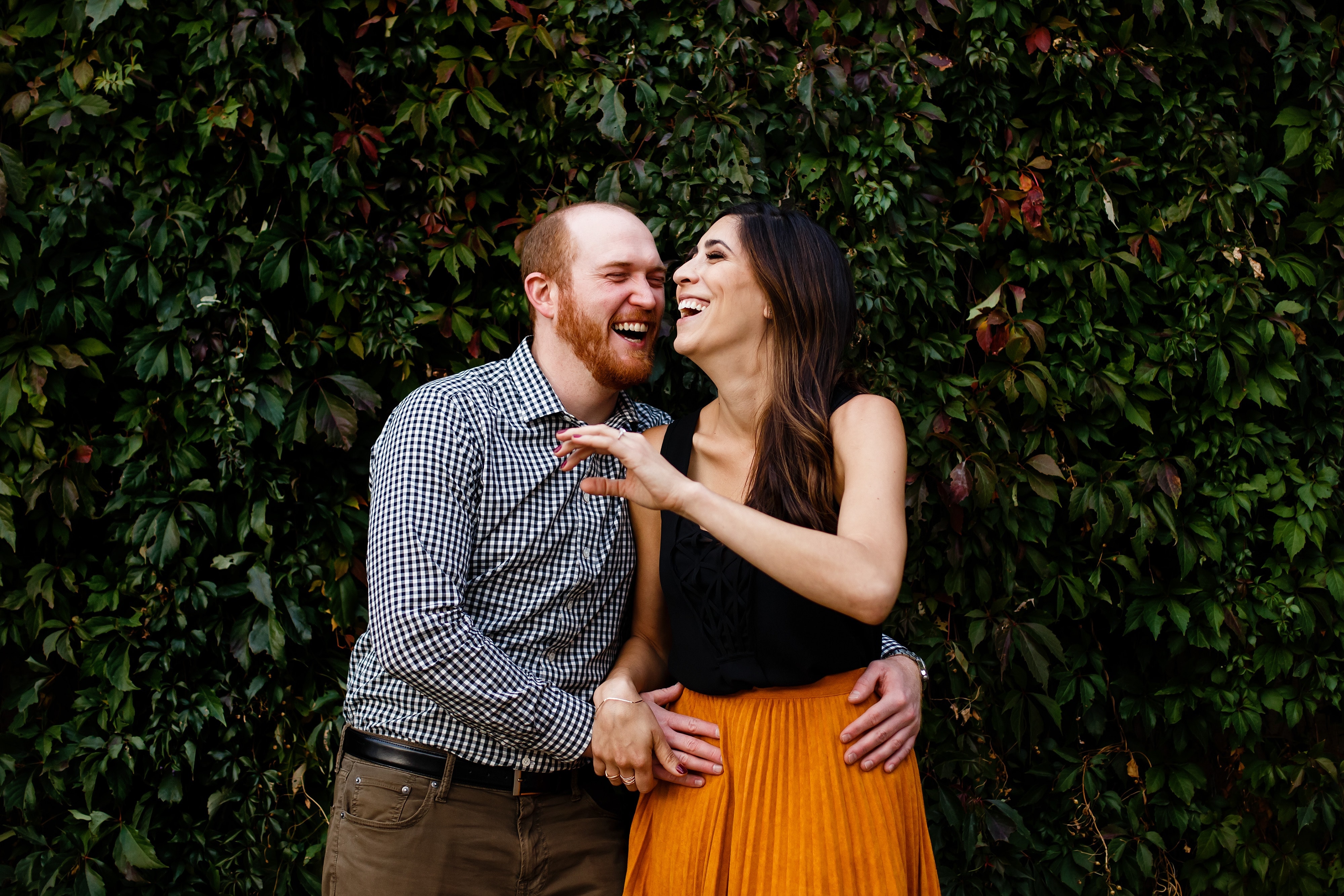 Chris and Angie share a laugh together in front of the ivy wall along the Cherry Creek path in Lower Downtown during their engagement session