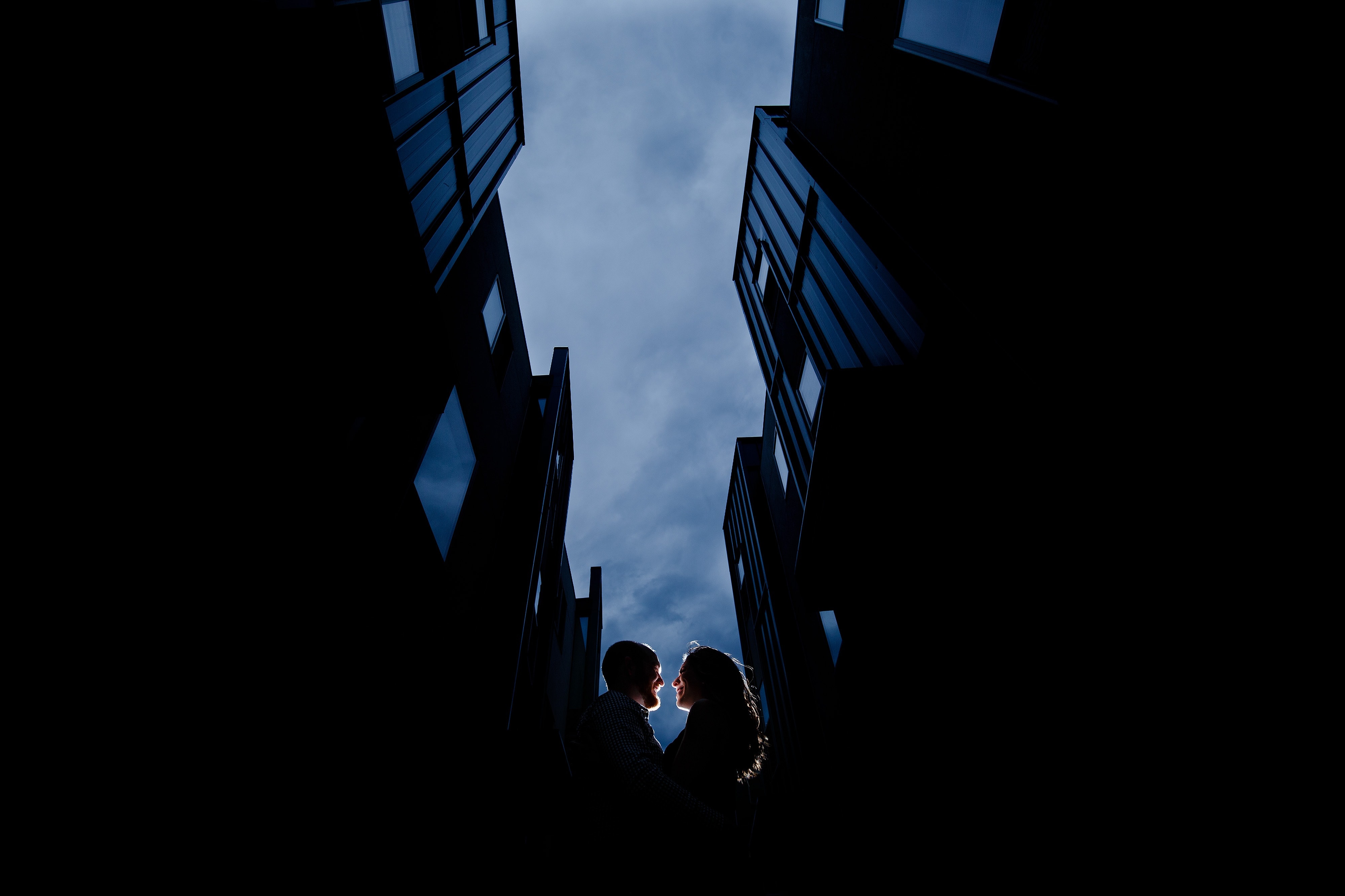 The couple is illuminated between condos in the Jefferson Park neighborhood of Denver during their engagement
