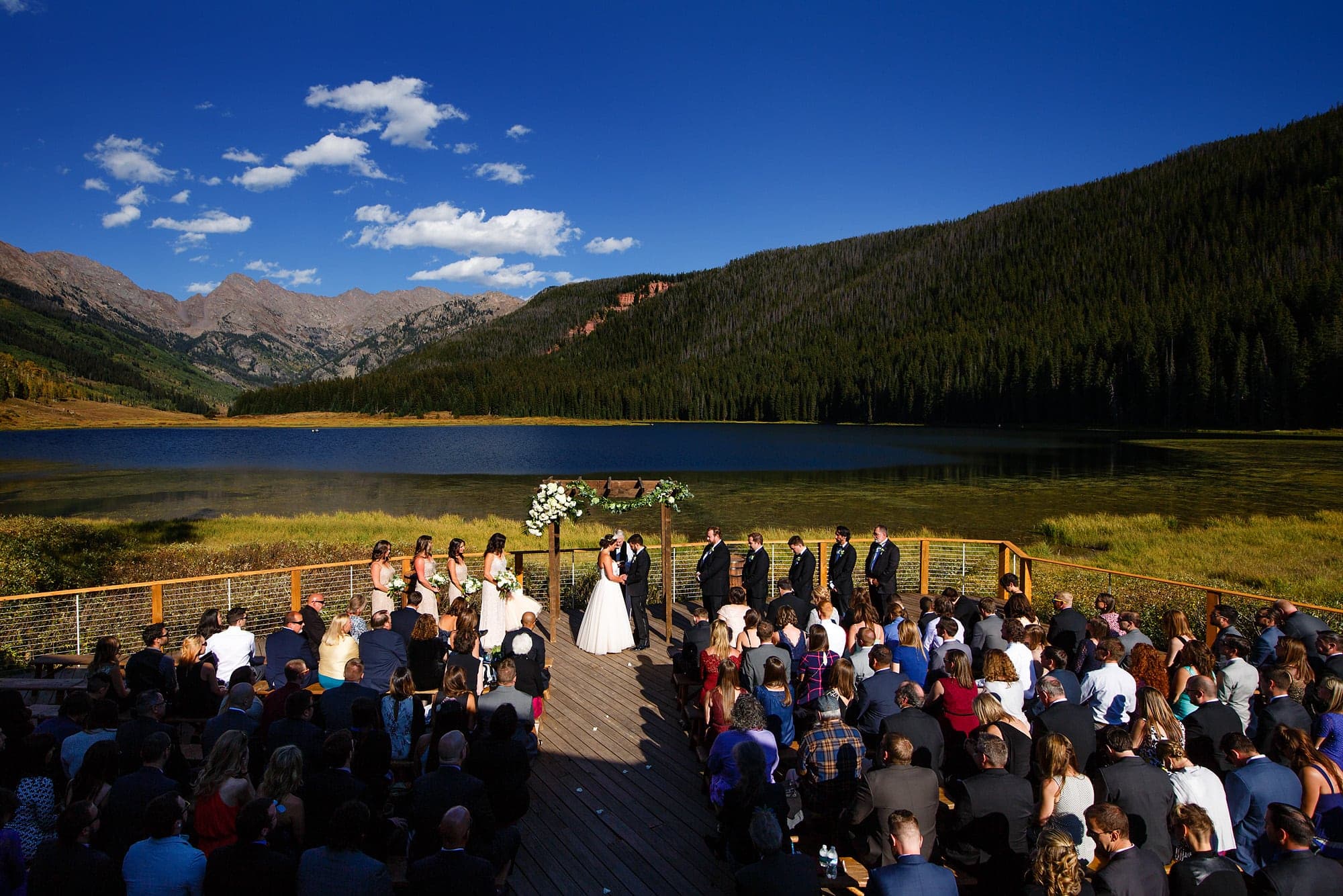The wedding ceremony takes place on the deck at Piney River Ranch in September 2016 outside of Vail, Colorado with the Gore mountain range in the background.