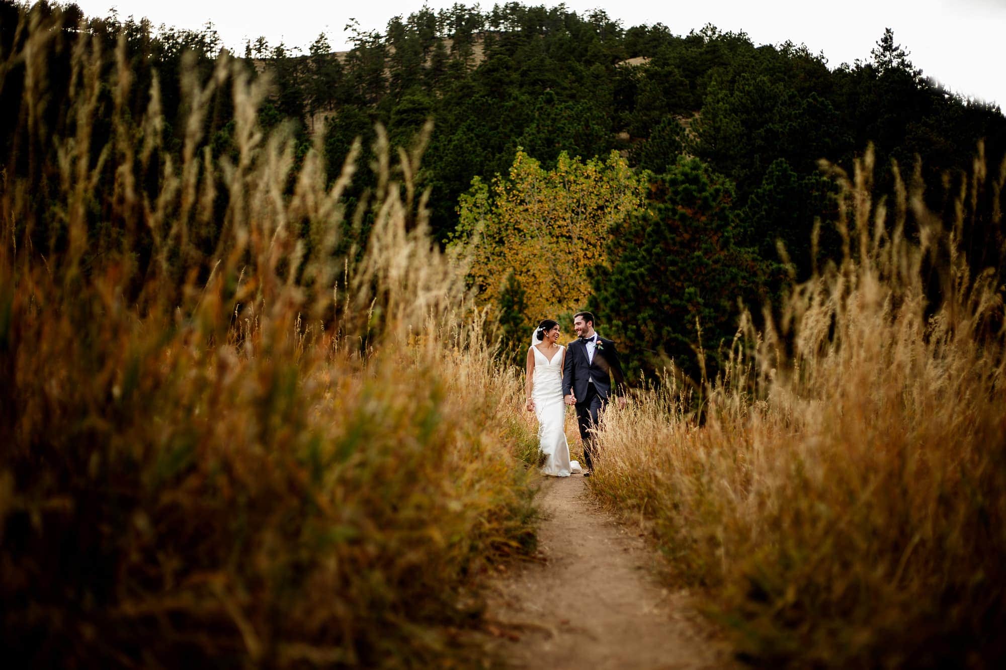 Megan walks with Bryan in the long grass at Centennial Park Trailhead in Boulder following their fall wedding