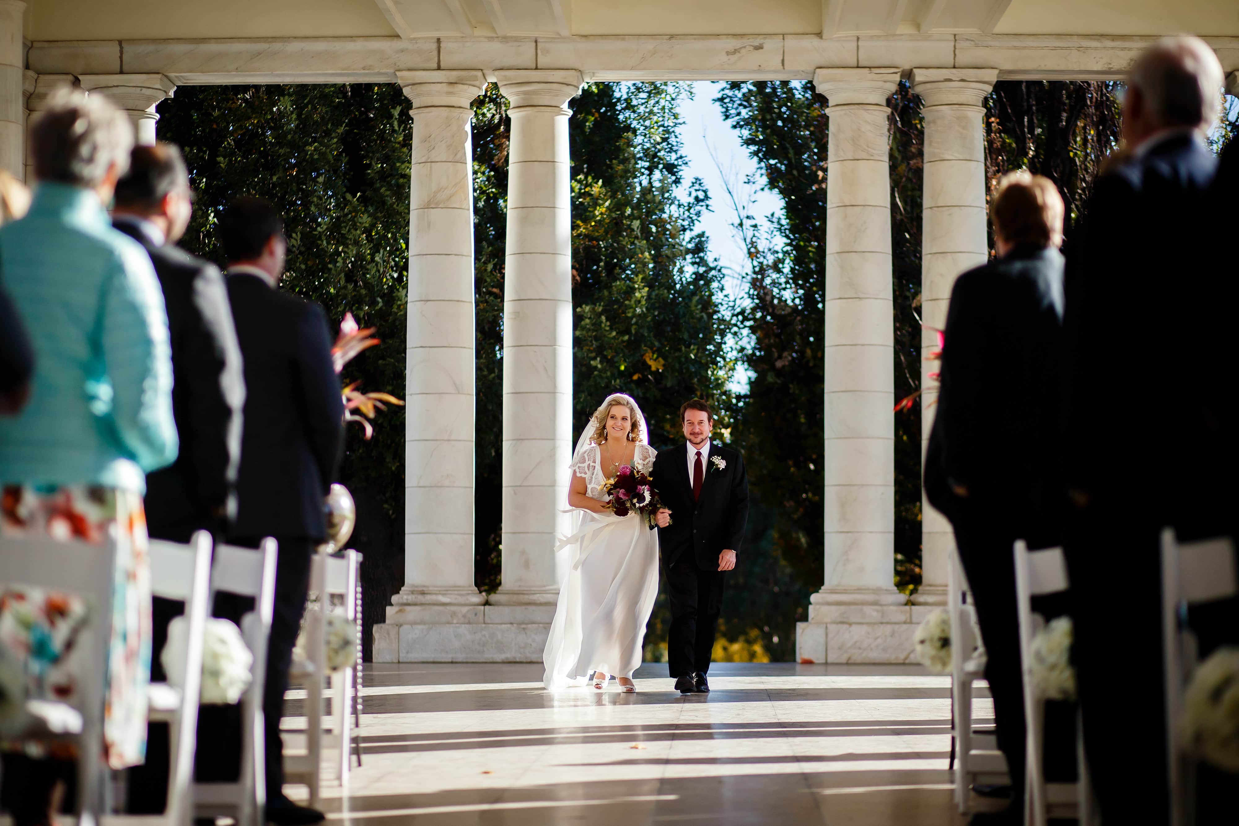 Sarah walks down the aisle with her father during her wedding at the pavillion at Cheesman Park in Denver