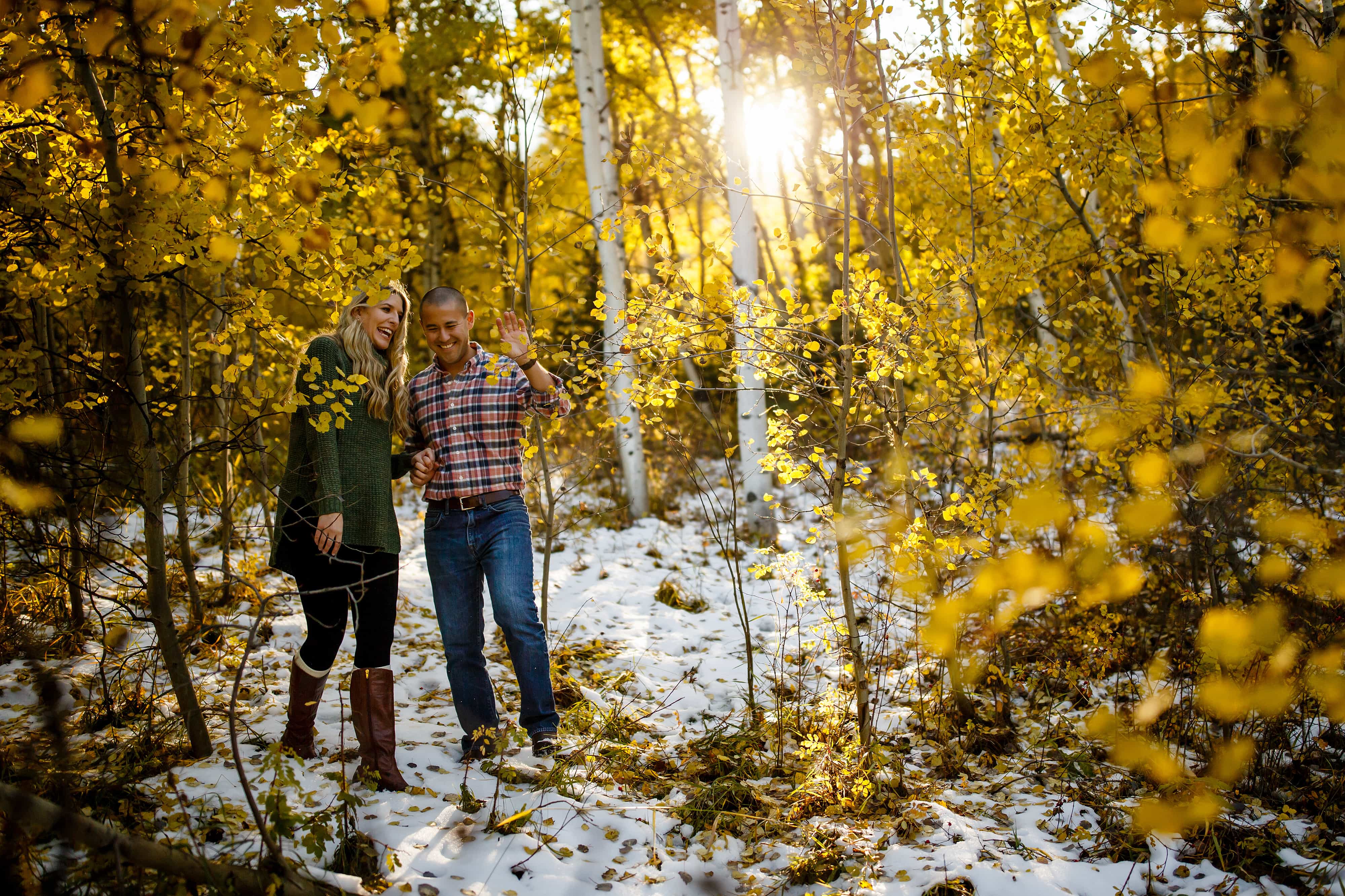 Adam pushes branches aside while walking with Paige through snow in a grove of yellow colored aspen trees during their Golden Gate Canyon State Park engagement photos
