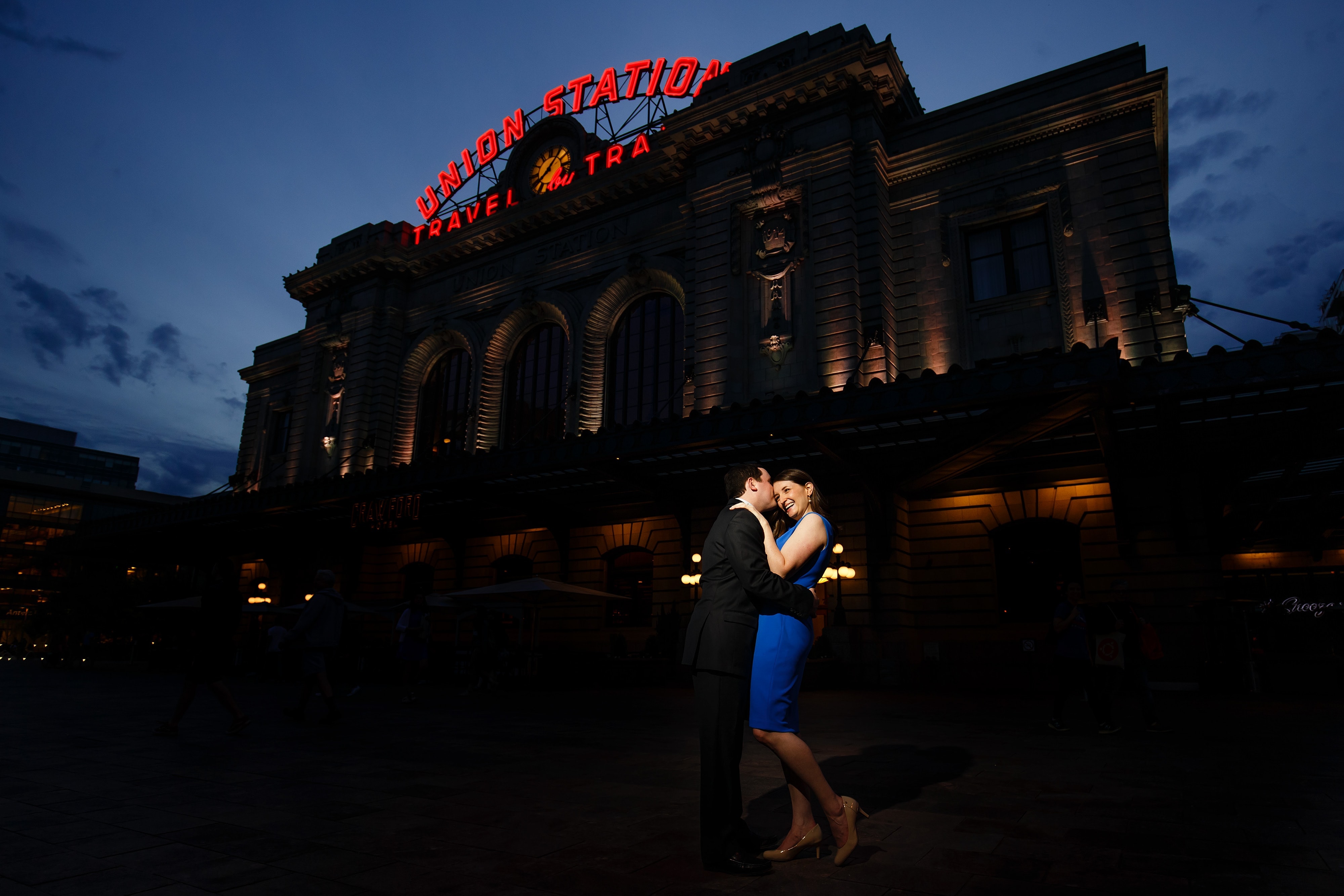 Joel kisses Katie in front of Denver's Union Station during their spring engagement session at twilight