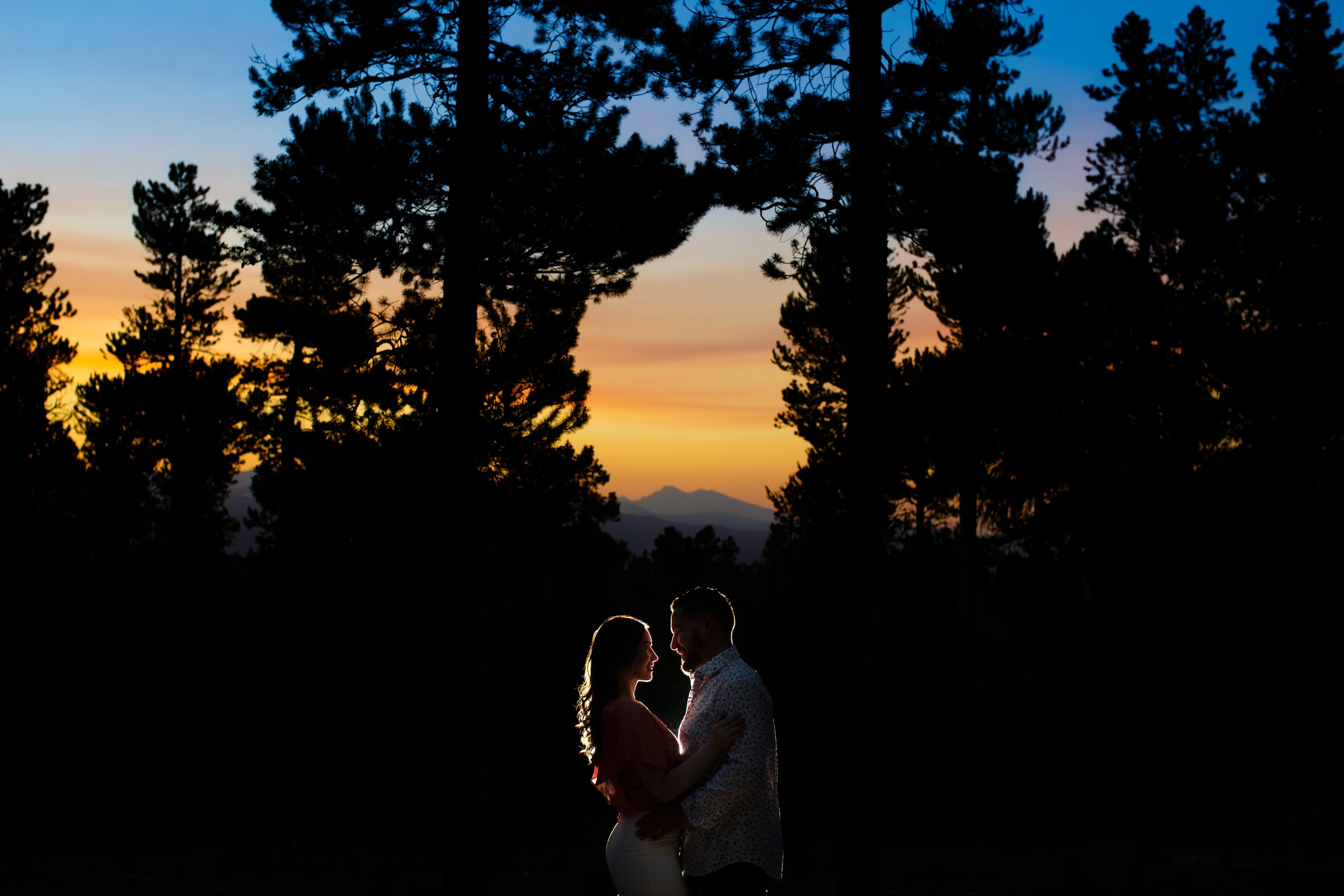Sharon and Nick embrace as the sun sets over the mountains during their colorful engagement in Golden Gate Canyon State Park