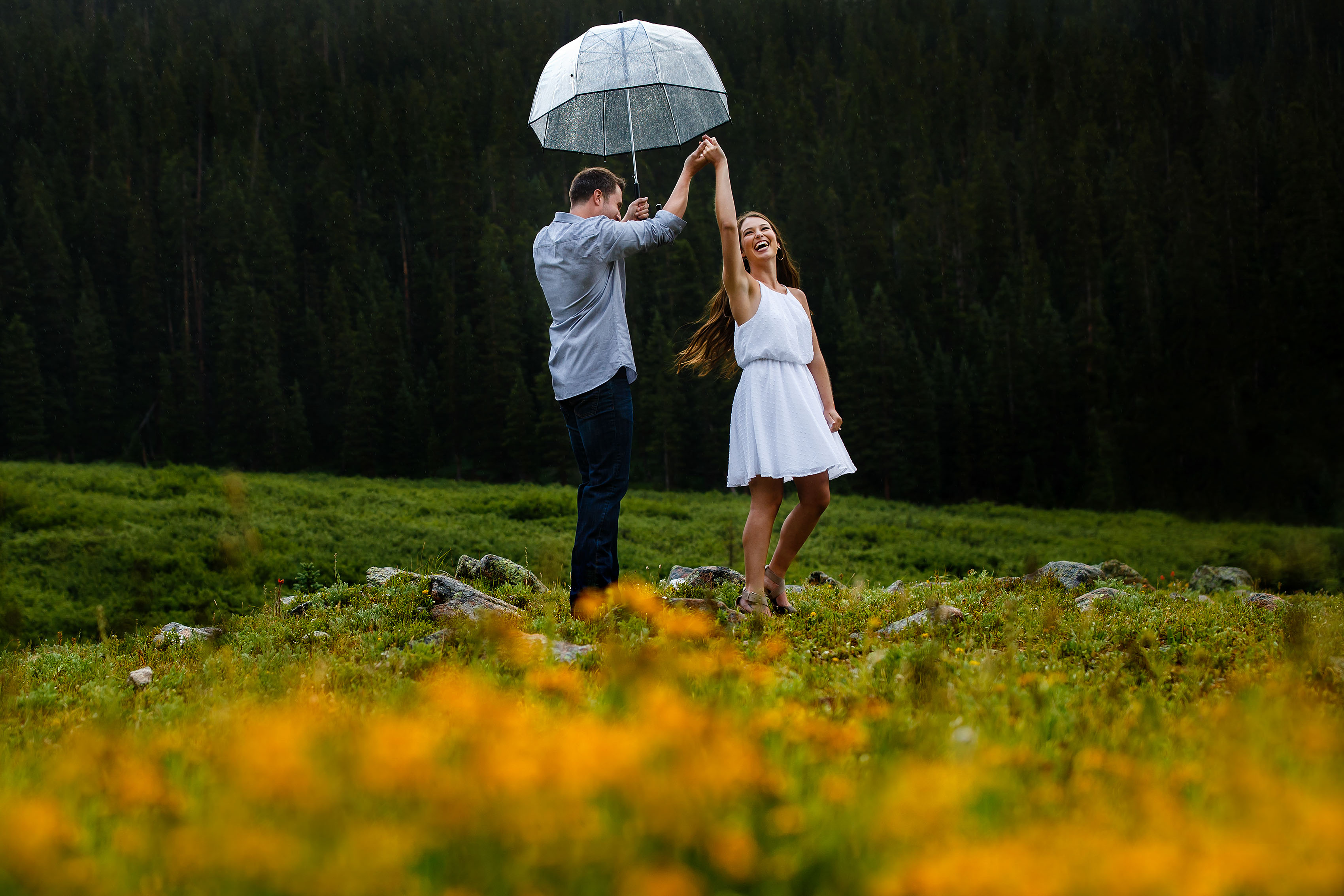 A couple dances in the rain near a patch of wildflowers during their Loveland Pass summer engagement session in Colorado