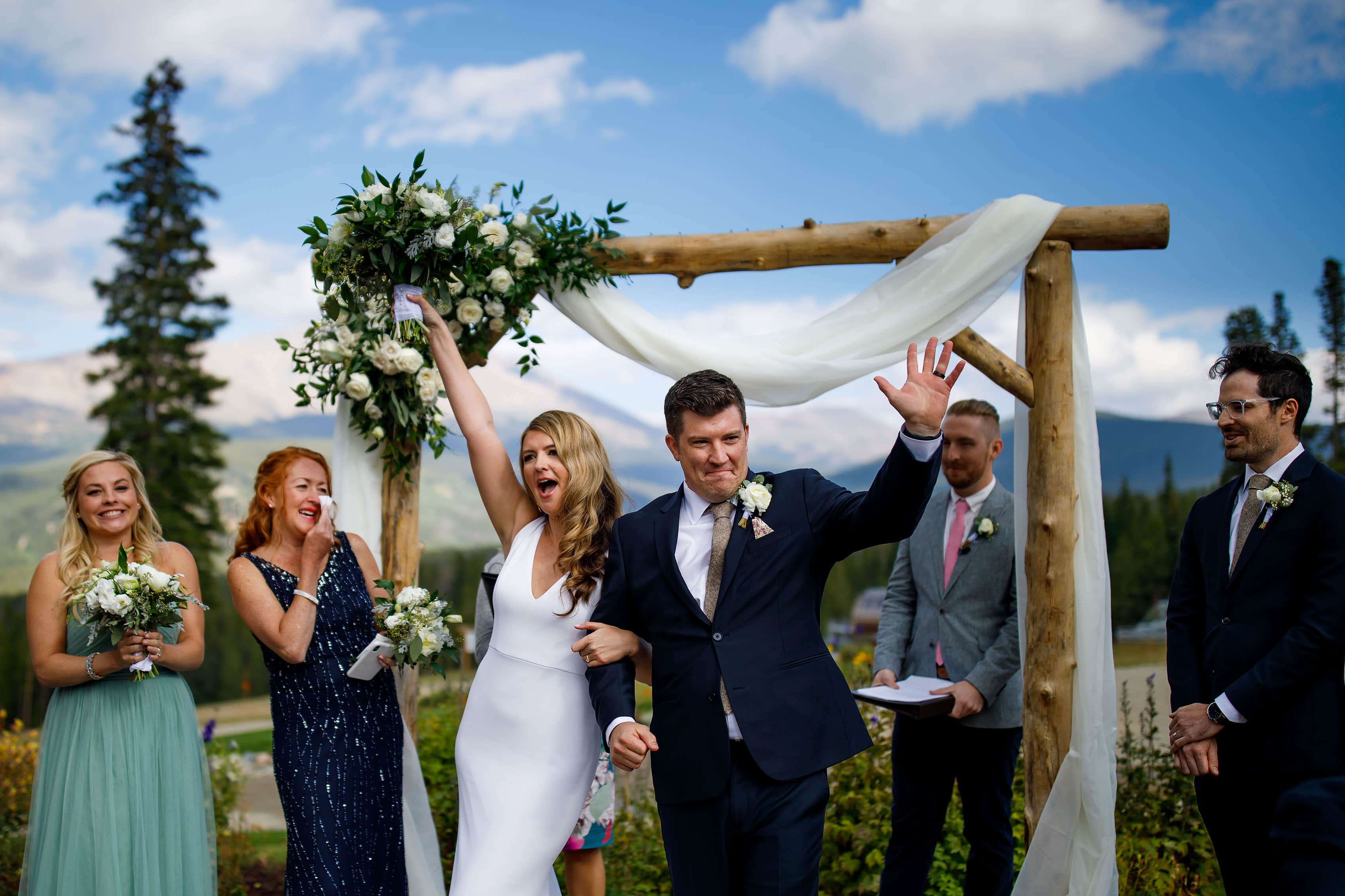 The bride and groom celebrate in front of a wooden arch with flowers at TenMile