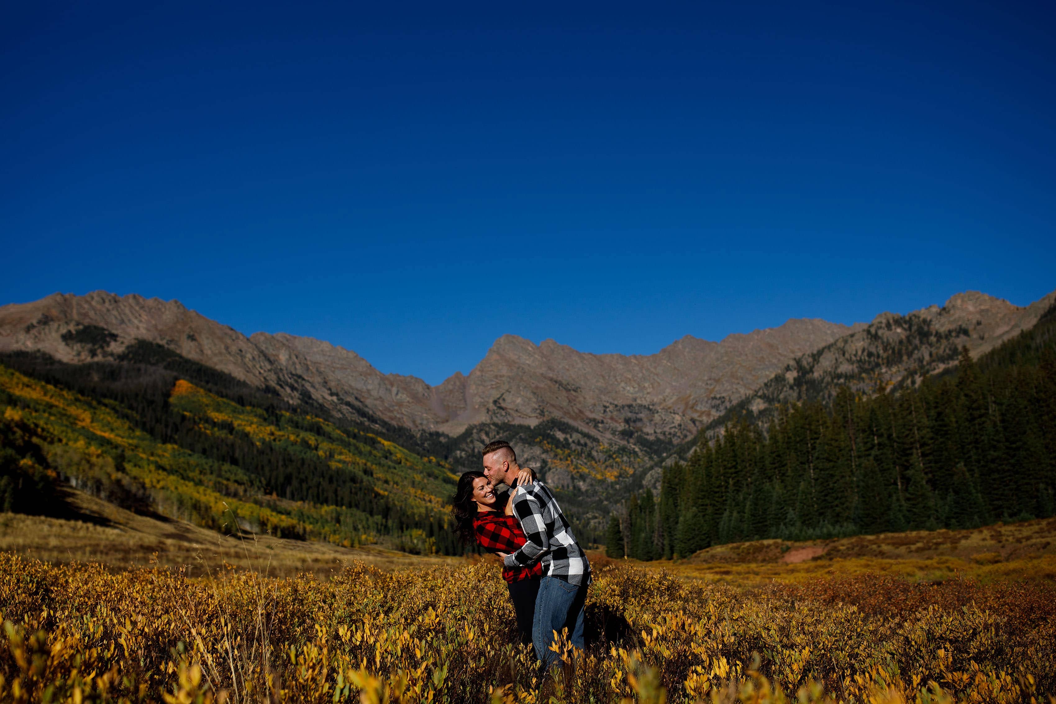 A couple poses in plaid flannel shirts during their fall Piney River Ranch engagement in front of the Gore mountain range near Vail Colorado