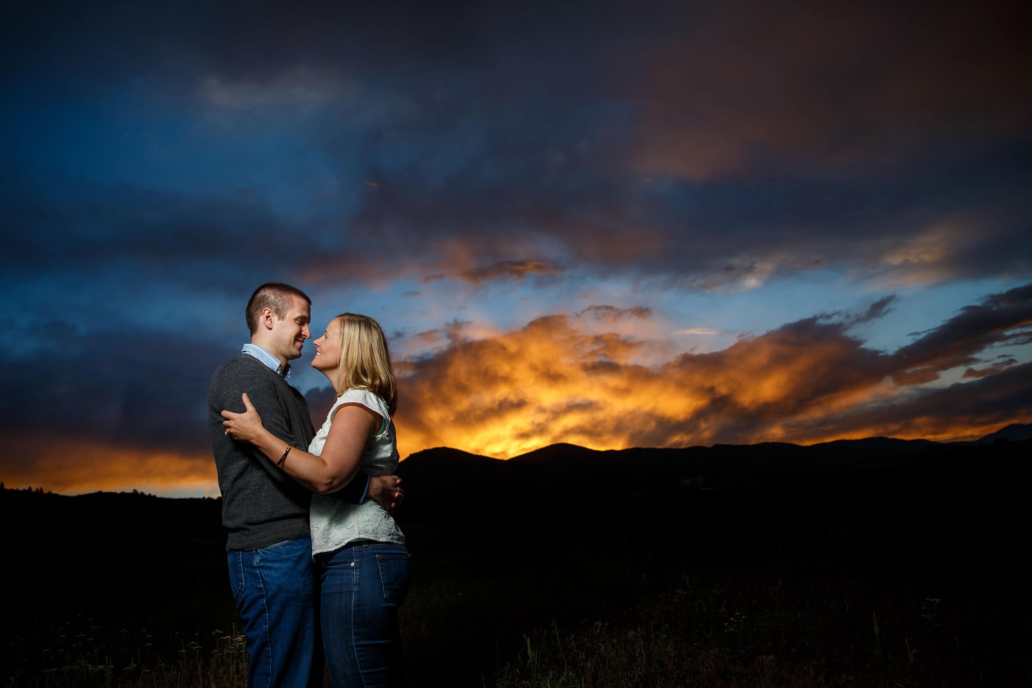 Ross and Emily embrace under a vibrant sunset during their Roxborough State Park engagement