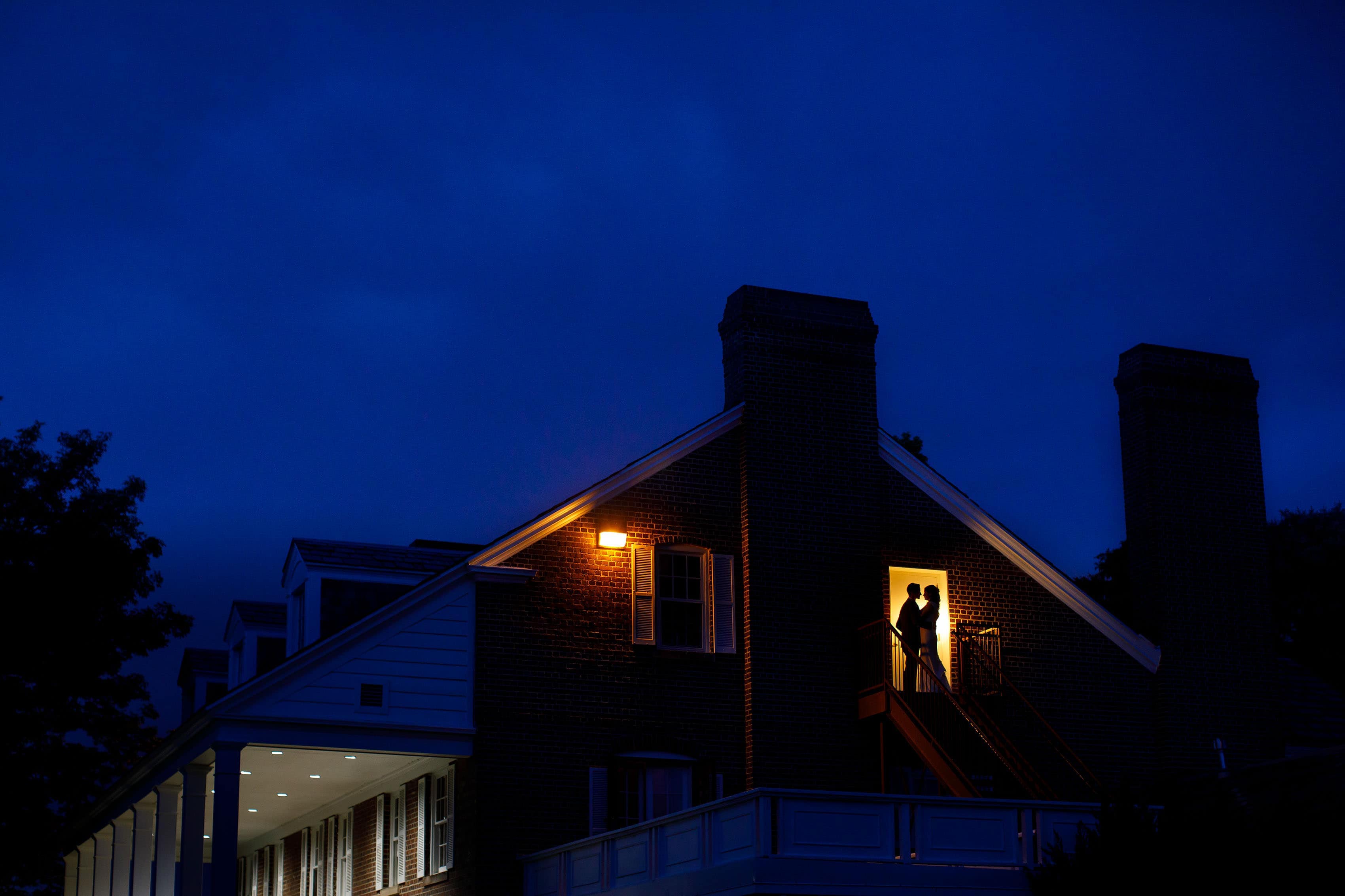 A couple are silhouetted against a balcony door at twilight during a Buell Mansion wedding ceremony