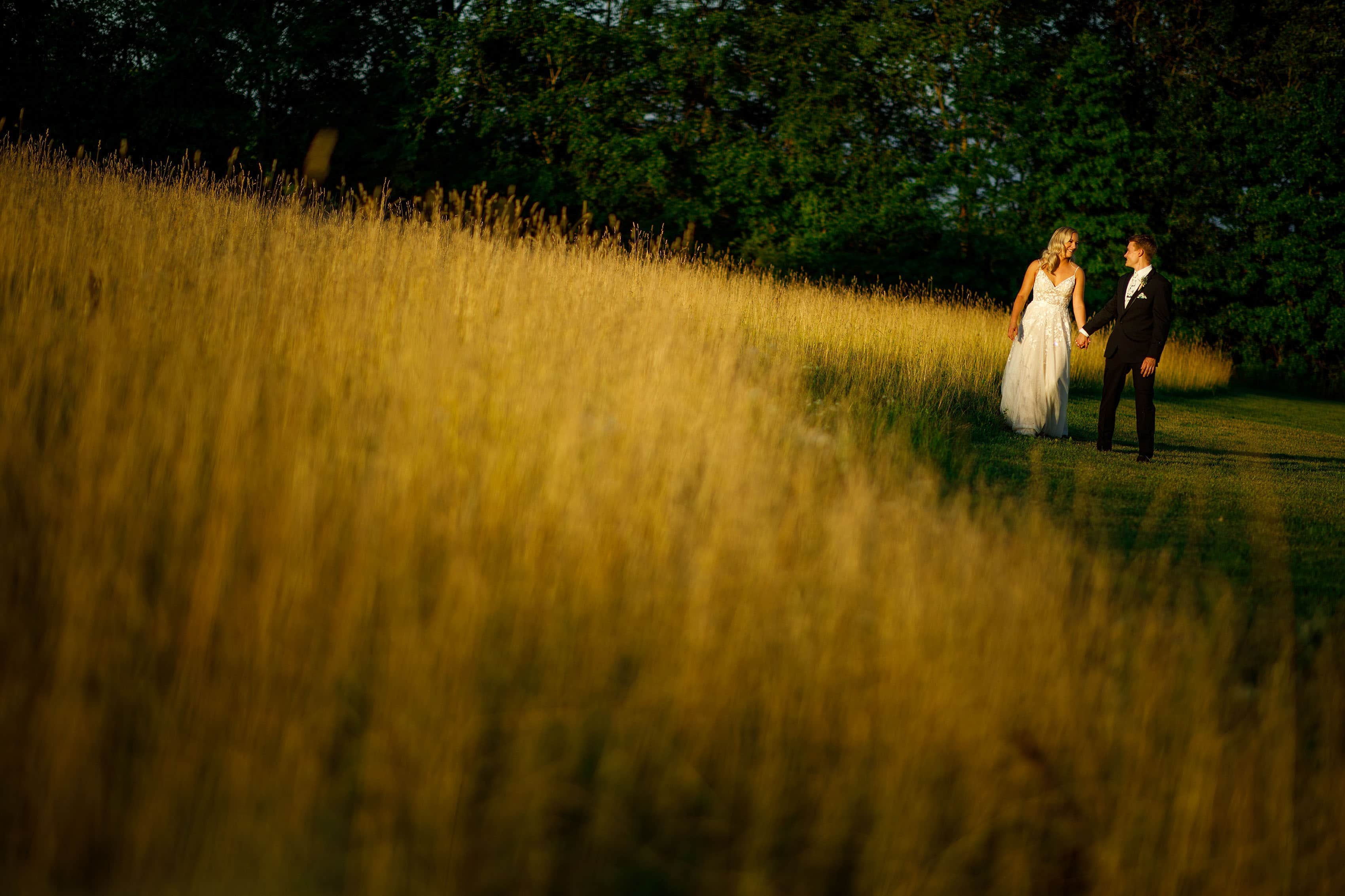 The newlyweds walk together at golden hour during their summer Emerson Fields wedding in Excello, Missouri