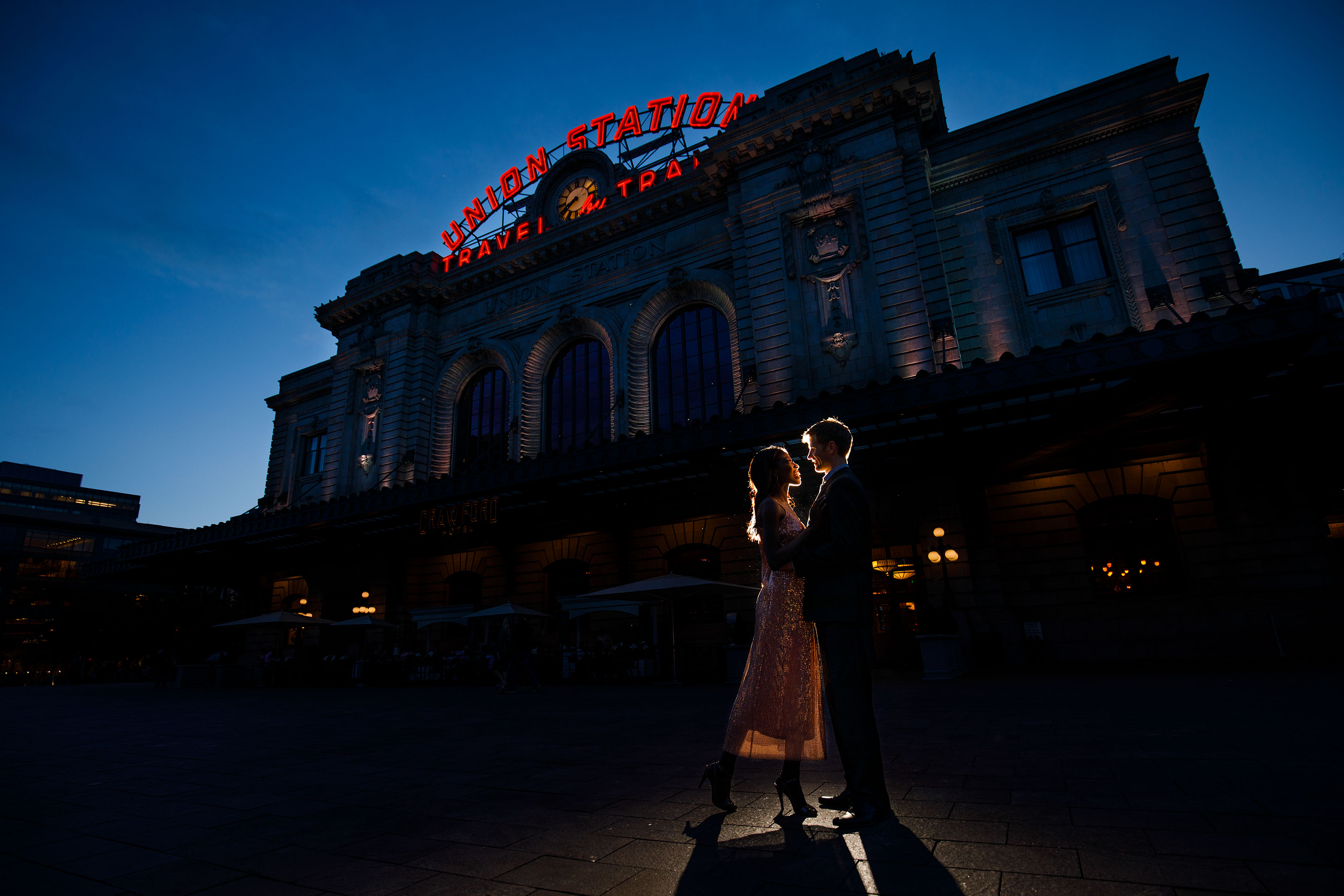 Ewo and Henry pose together at twilight in front of Denver Union Station during their engagement photos