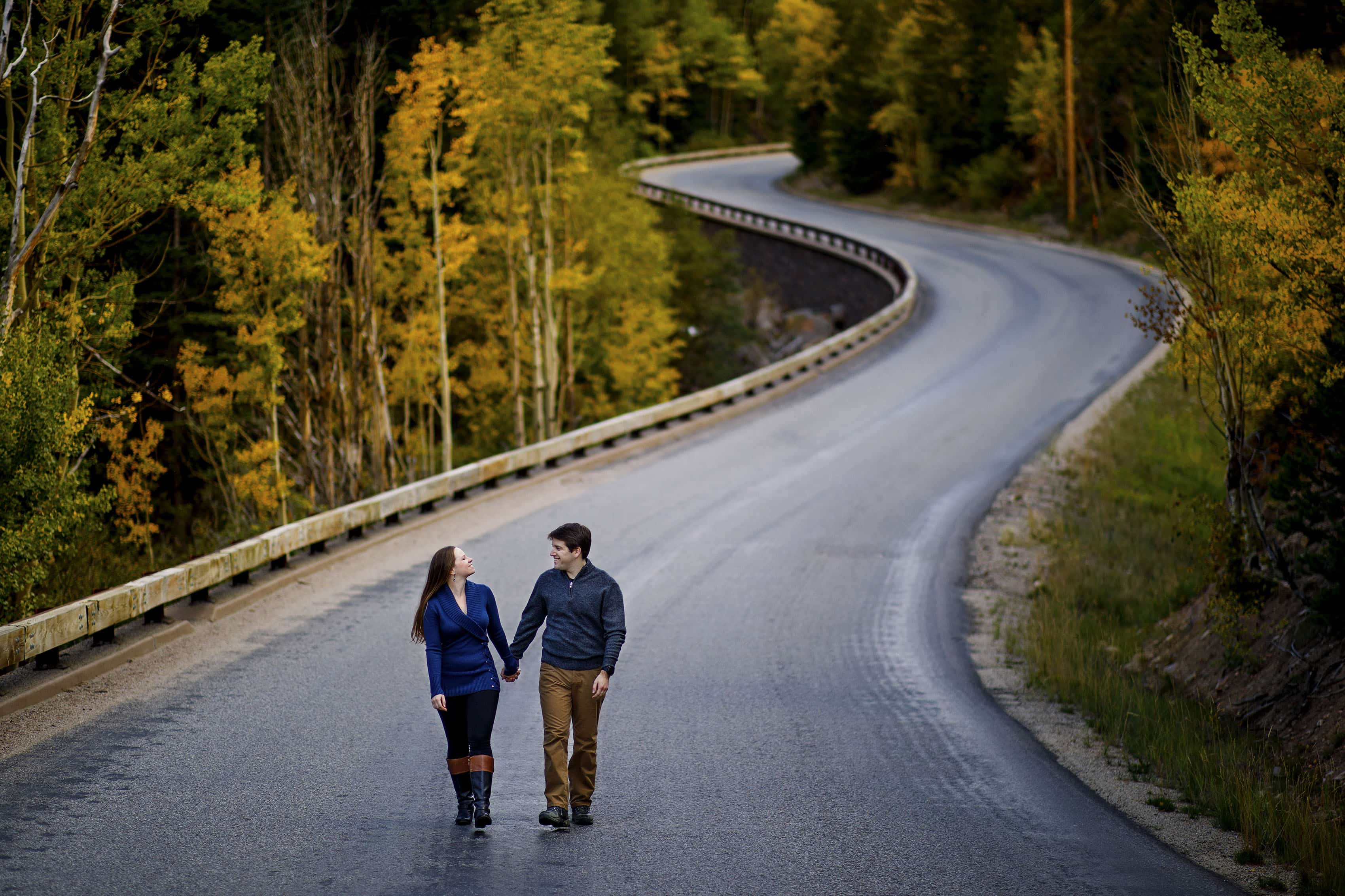 A couple walk together on Guanella Pass road lined with changing aspen trees during their fall engagement session