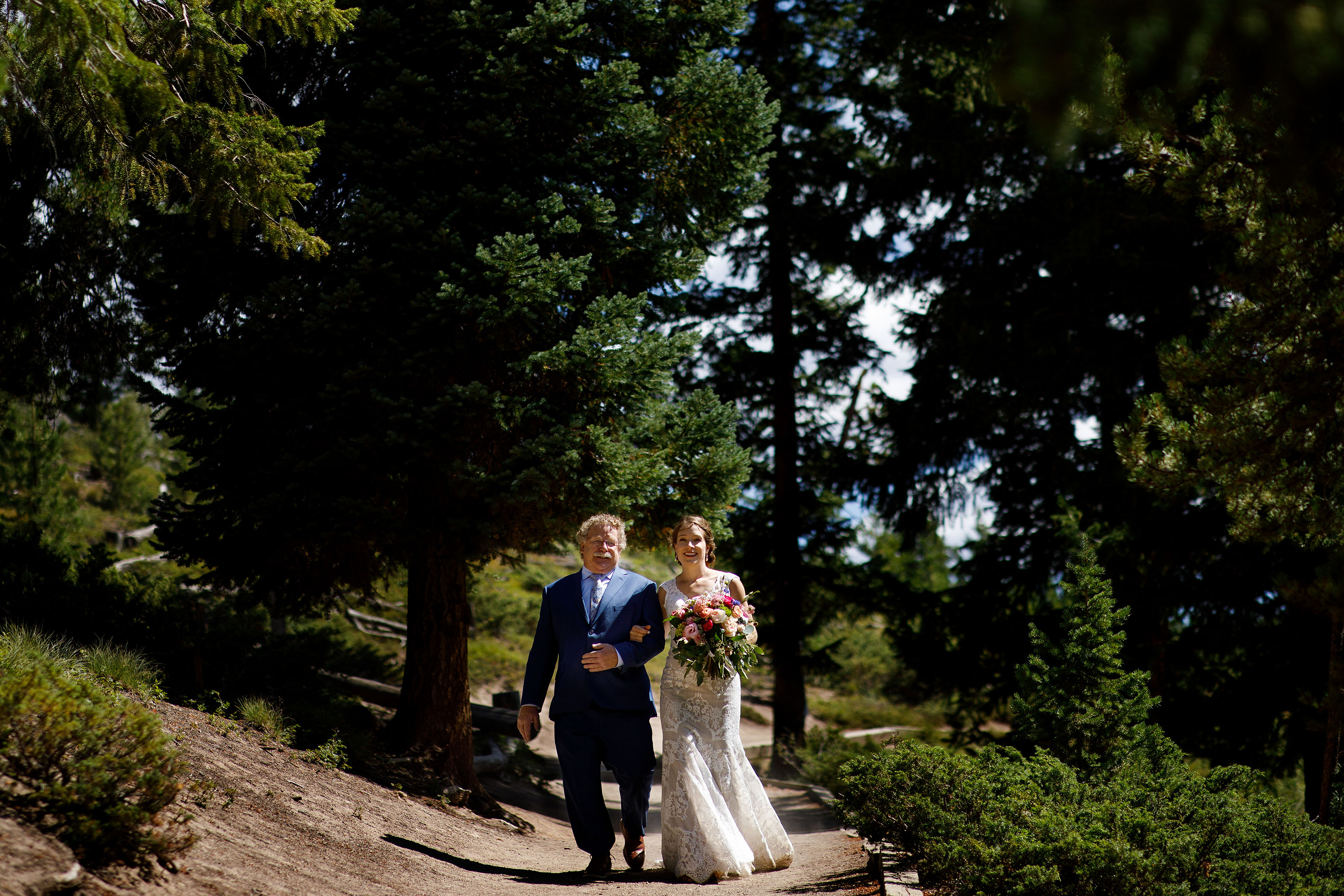 The bride walks down the path with her father at Sapphire Point