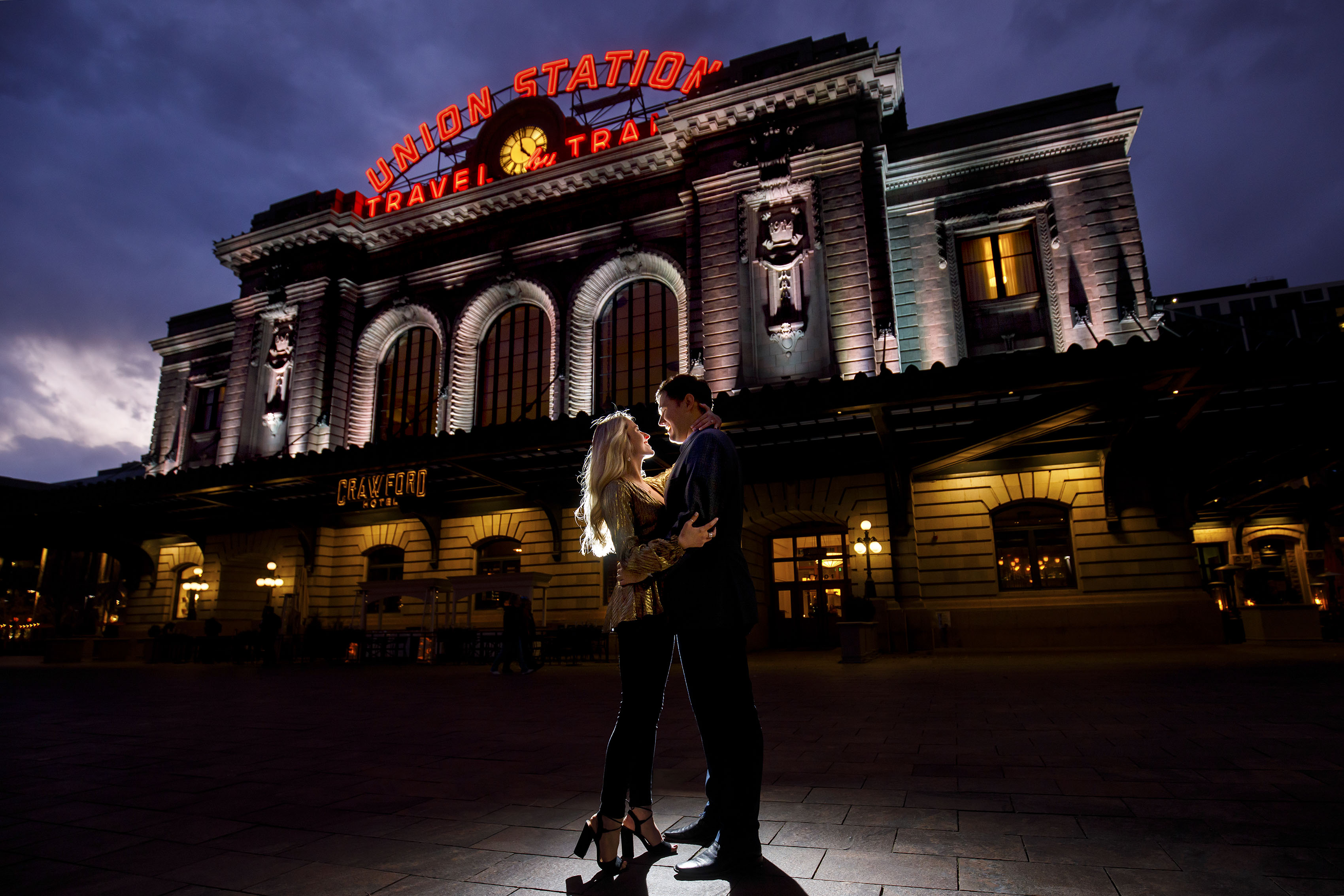 Sierra and Alex pose outside Denver's Union Station during twilight as they celebrate their recent engagement