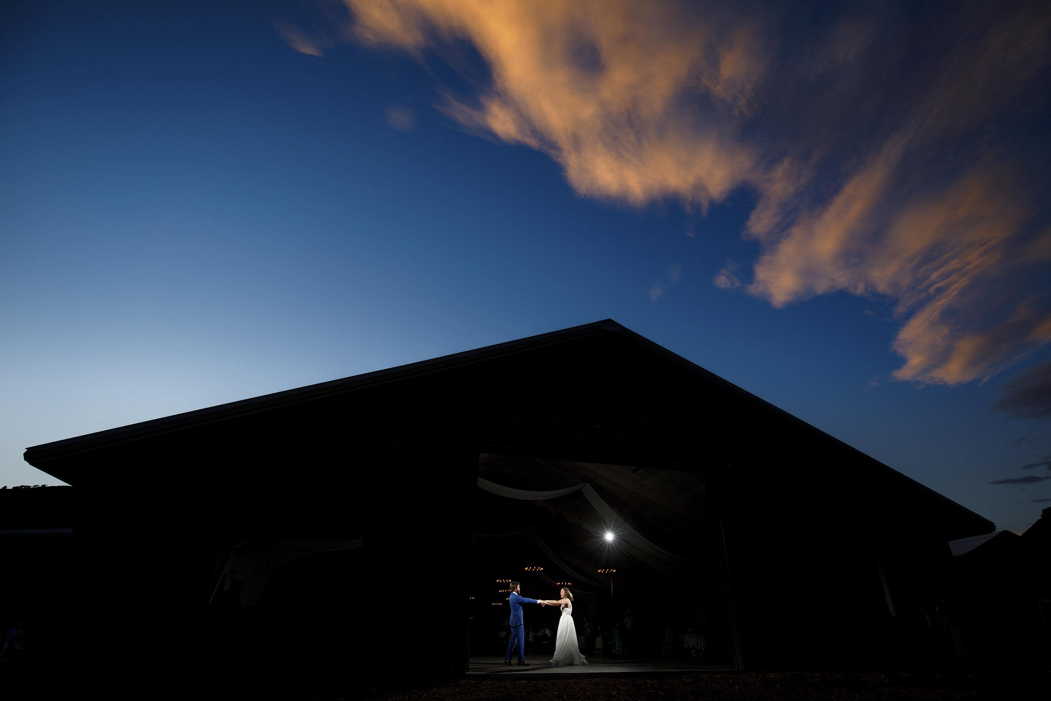 Laura and Ryan dance together in the barn as the sunset illuminates clouds during their 4 Eagle Ranch wedding in Wolcott, CO