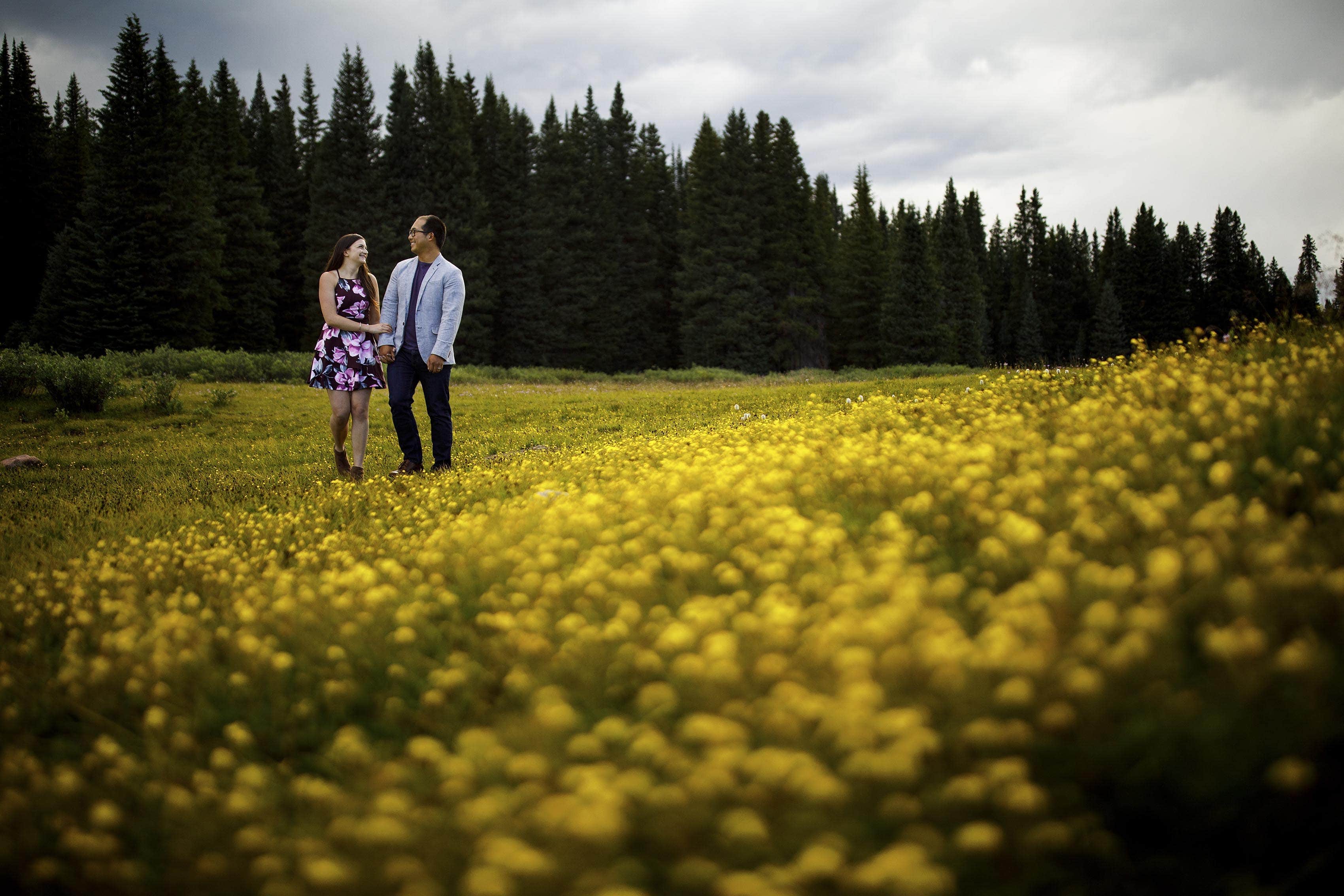 Courtney and Mike walk through a field of yellow wild flowers during their Shrine Pass engagement session in Colorado