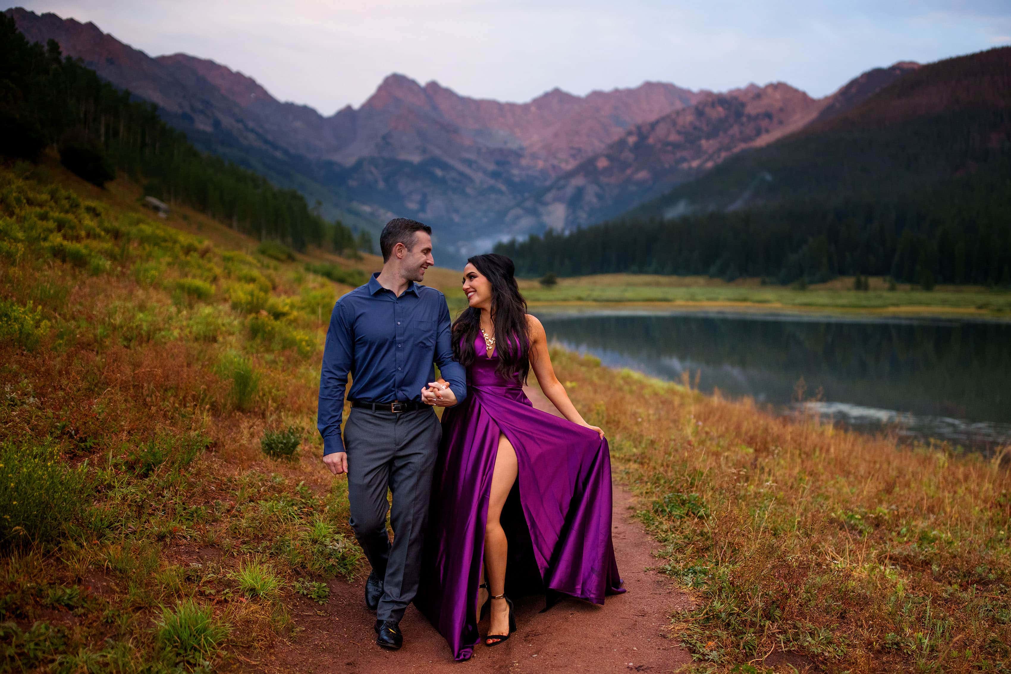 Maggie holds her purple gown as the alpenglow hits the Gore Range during their engagement photos at Piney Lake